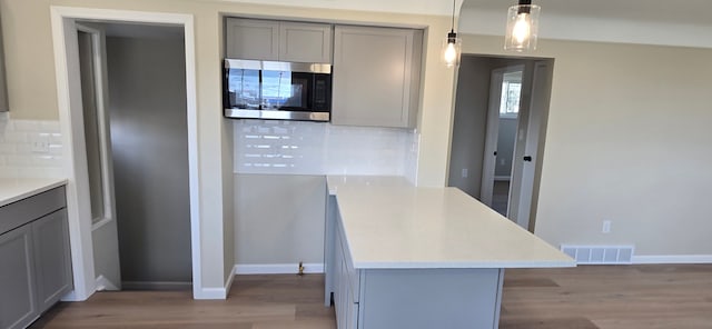 kitchen featuring stainless steel microwave, visible vents, gray cabinets, and decorative backsplash