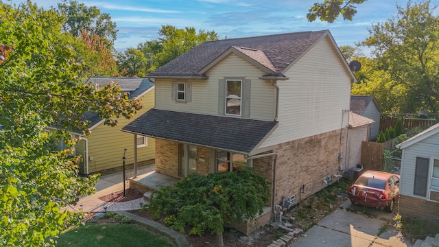 view of front of home featuring brick siding, a shingled roof, and fence