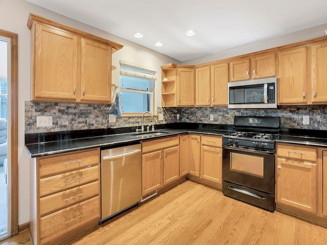 kitchen with dark countertops, stainless steel appliances, light wood finished floors, and a sink