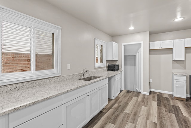 kitchen featuring a sink, light wood-type flooring, white cabinetry, light stone countertops, and black microwave