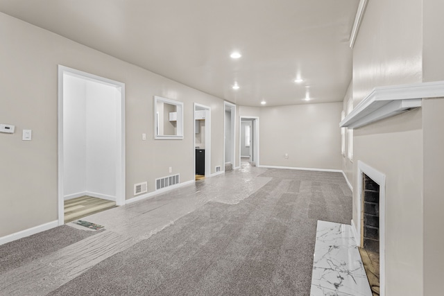 unfurnished living room featuring recessed lighting, a high end fireplace, visible vents, and light carpet