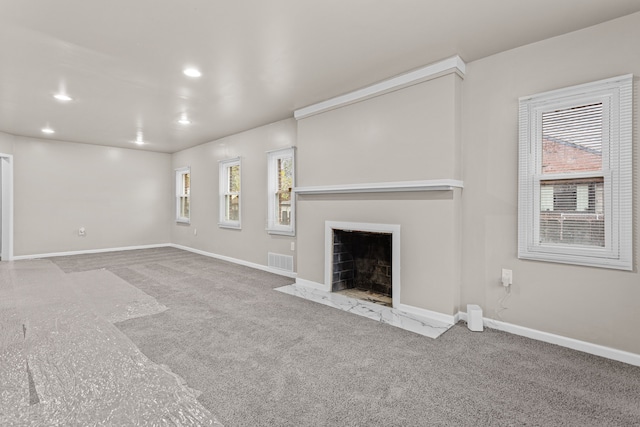 unfurnished living room featuring a fireplace with flush hearth, carpet floors, visible vents, and baseboards