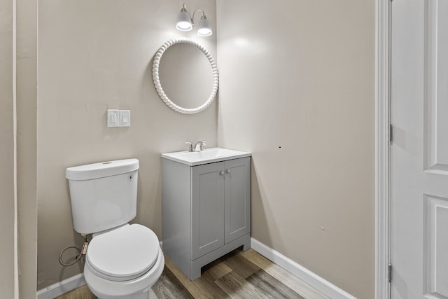 half bath with baseboards, toilet, vanity, and wood finished floors