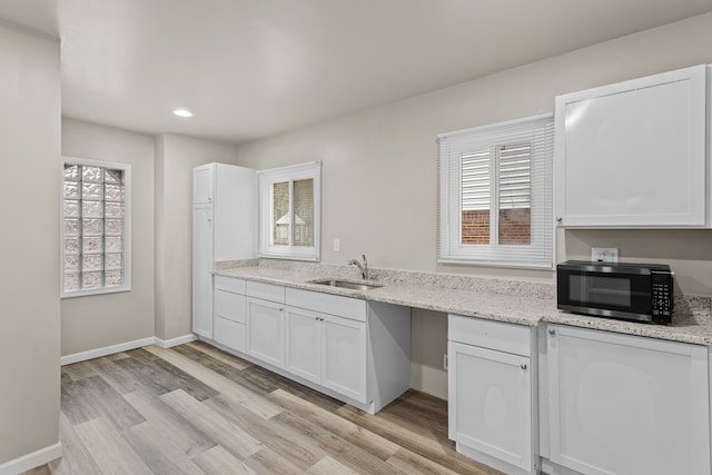 kitchen with light wood-type flooring, a sink, and white cabinetry