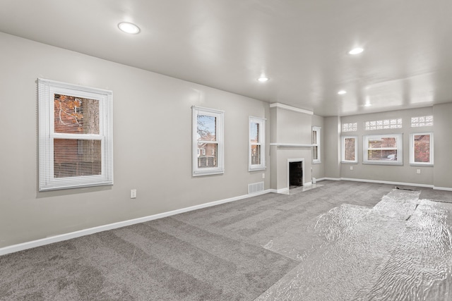 unfurnished living room with recessed lighting, a healthy amount of sunlight, visible vents, and carpet