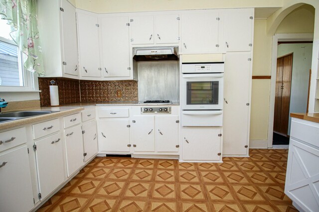 kitchen featuring light floors, white oven, under cabinet range hood, and a warming drawer