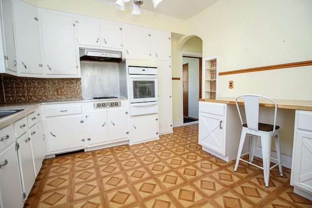 kitchen with oven, arched walkways, light countertops, white cabinets, and under cabinet range hood