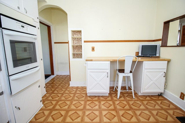 kitchen featuring white oven, wood counters, a warming drawer, light floors, and white cabinetry