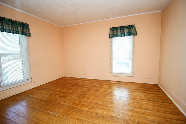 empty room with plenty of natural light, wood finished floors, a textured ceiling, and ornamental molding