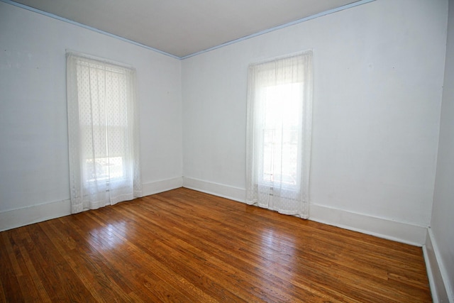spare room with baseboards, wood finished floors, and crown molding