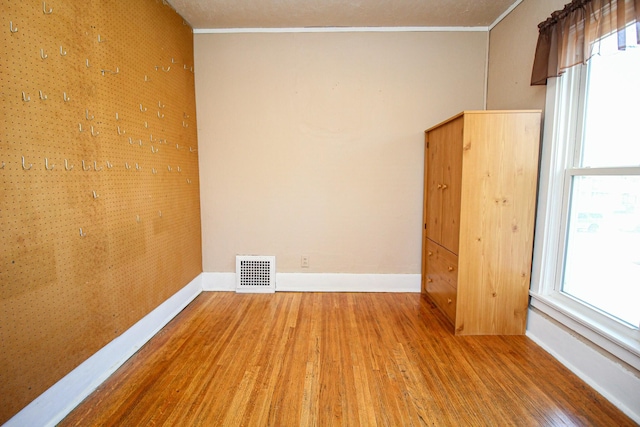 unfurnished room featuring wood finished floors, visible vents, crown molding, and baseboards