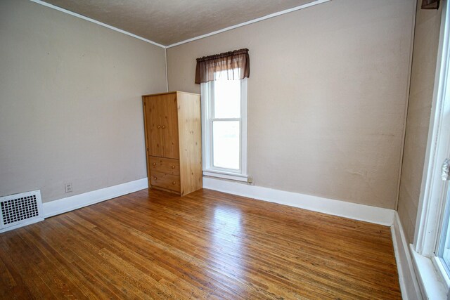 empty room featuring baseboards, wood finished floors, visible vents, and ornamental molding