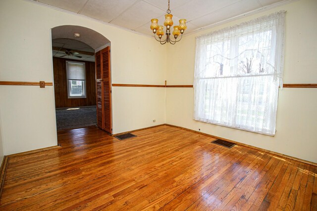 unfurnished room featuring wood-type flooring, arched walkways, visible vents, and ceiling fan with notable chandelier