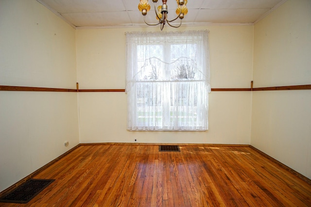 empty room with crown molding, a notable chandelier, hardwood / wood-style floors, and visible vents