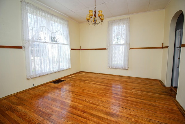 empty room with a healthy amount of sunlight, wood finished floors, and a chandelier