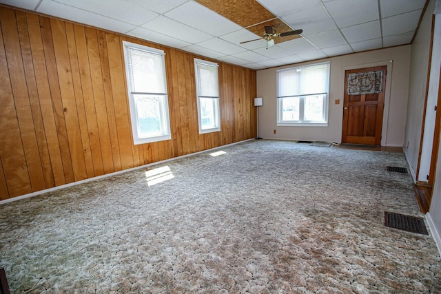 unfurnished living room featuring carpet, wood walls, visible vents, a ceiling fan, and a paneled ceiling
