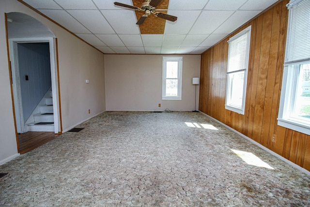 spare room featuring stairway, wood walls, arched walkways, baseboards, and ceiling fan