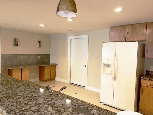 kitchen featuring white refrigerator with ice dispenser, recessed lighting, brown cabinets, and dark stone counters