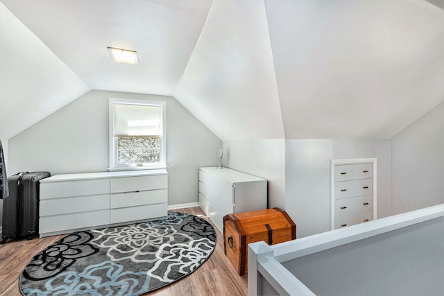 bedroom with light wood-type flooring, vaulted ceiling, and radiator