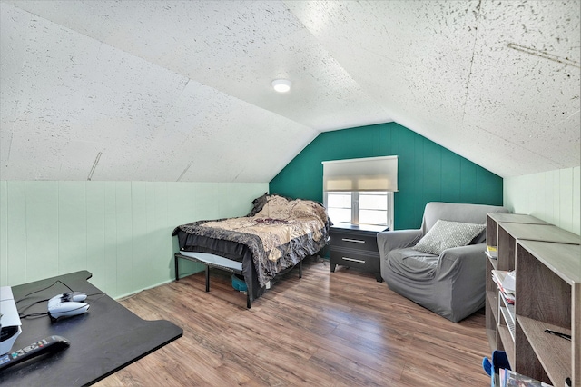 bedroom with lofted ceiling, wood finished floors, and a textured ceiling
