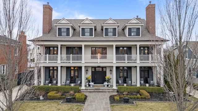 view of front facade with covered porch, french doors, a chimney, and a balcony