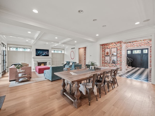 dining room with a warm lit fireplace, ornamental molding, beam ceiling, and light wood-type flooring