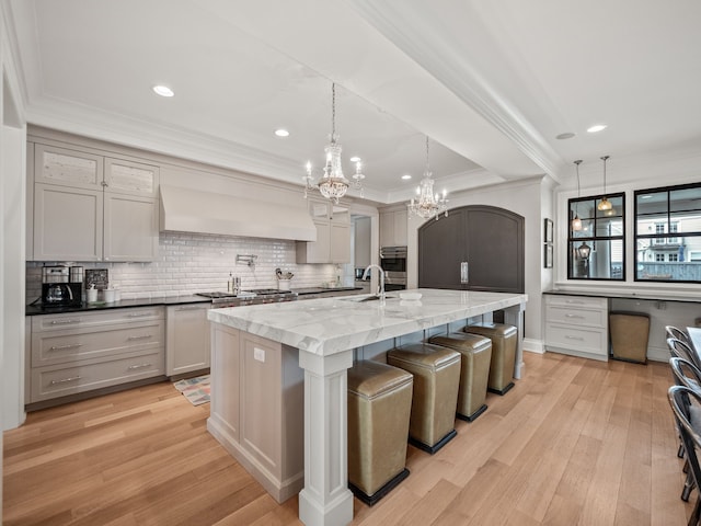 kitchen with light wood-type flooring, custom exhaust hood, an inviting chandelier, and ornamental molding