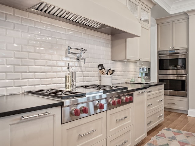 kitchen featuring tasteful backsplash, light wood-style floors, glass insert cabinets, stainless steel appliances, and premium range hood