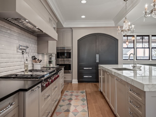 kitchen featuring stainless steel appliances, a sink, light wood-type flooring, decorative backsplash, and custom range hood