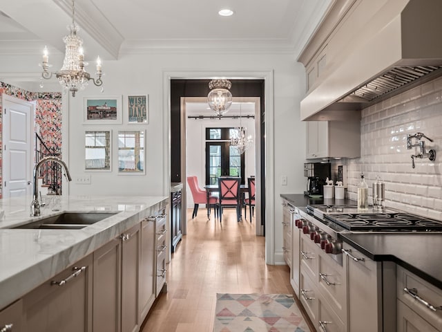 457 Catalpa Dr, Birmingham, MI 48009 - kitchen with a chandelier, wall chimney range hood, a sink, light wood-type flooring, and stainless steel gas stovetop