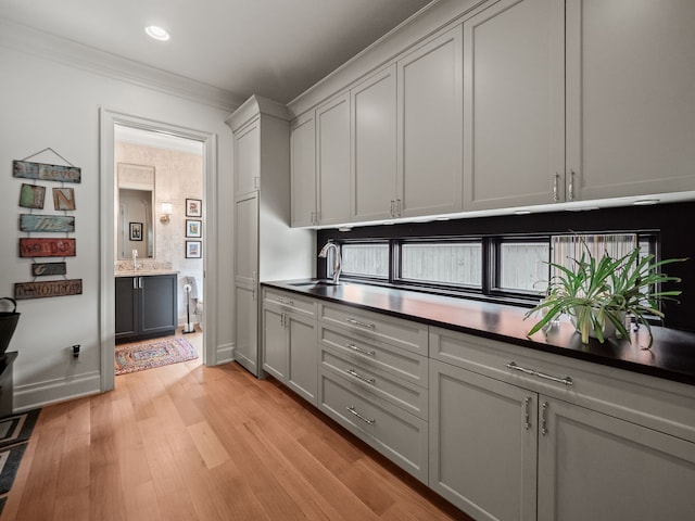 kitchen featuring recessed lighting, a sink, light wood-style floors, crown molding, and baseboards