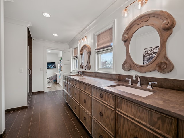 bathroom with crown molding, a sink, double vanity, baseboards, and recessed lighting