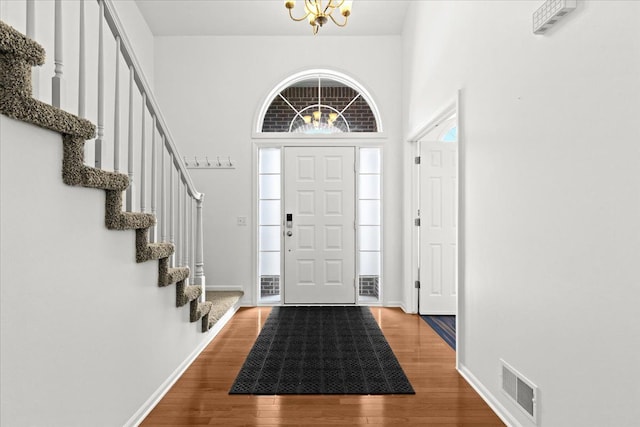 entryway with visible vents, an inviting chandelier, stairs, wood finished floors, and baseboards