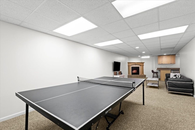 game room with carpet floors, a paneled ceiling, baseboards, and a lit fireplace