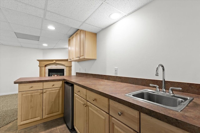 kitchen with a peninsula, light brown cabinets, dark countertops, a paneled ceiling, and a sink