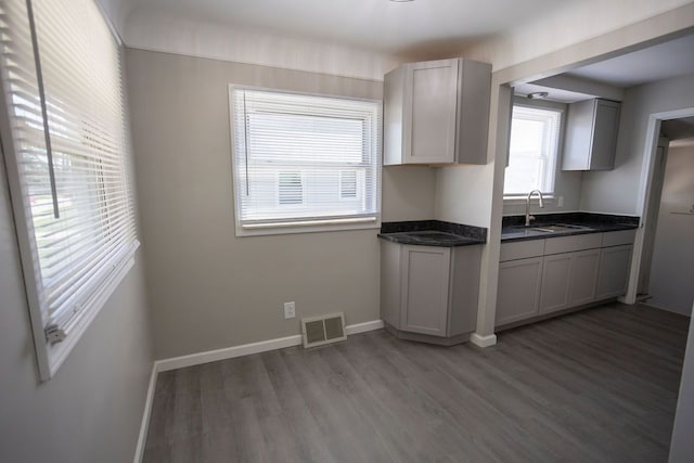 kitchen featuring light wood-style flooring, a sink, dark countertops, visible vents, and baseboards