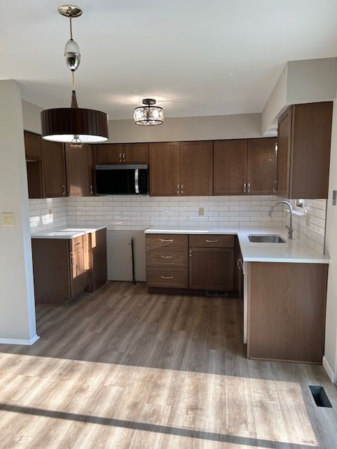 kitchen with a sink, stainless steel microwave, decorative backsplash, wood finished floors, and pendant lighting