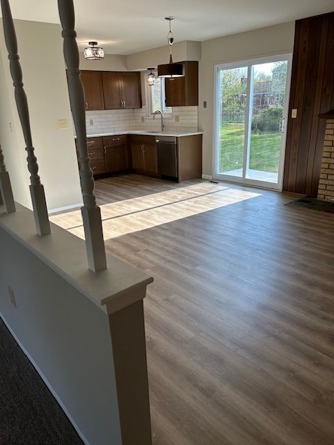 kitchen with a sink, dishwasher, light countertops, wood finished floors, and tasteful backsplash