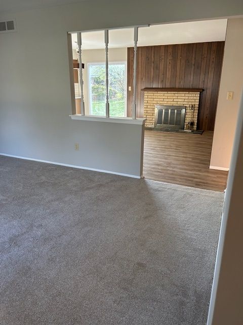 unfurnished living room featuring carpet flooring, baseboards, wood walls, and visible vents