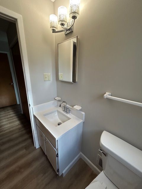 half bath with vanity, wood finished floors, a notable chandelier, and toilet