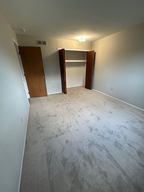 unfurnished bedroom with baseboards, light carpet, and visible vents