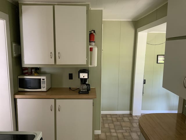 kitchen with ornamental molding, white cabinetry, stone finish floor, and white microwave