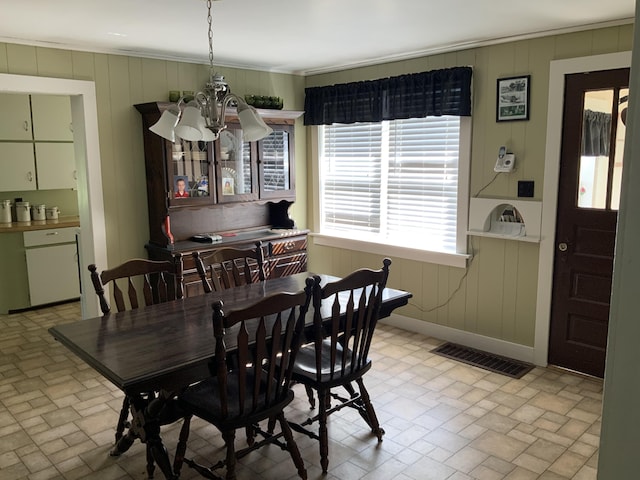 dining room with an inviting chandelier, visible vents, a decorative wall, and brick patterned floor