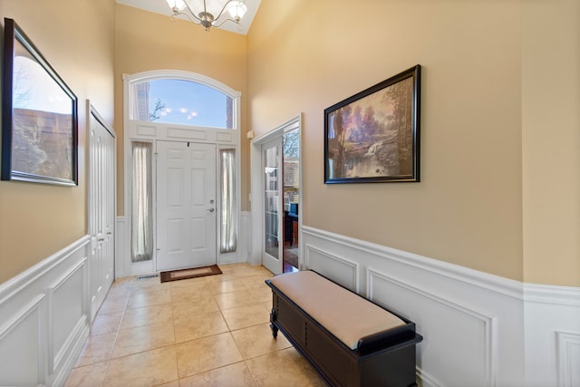 foyer entrance featuring light tile patterned flooring, a decorative wall, a notable chandelier, and wainscoting