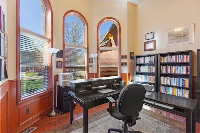 office area featuring a high ceiling, a wainscoted wall, wood finished floors, and visible vents