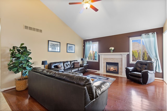 living area featuring high vaulted ceiling, ceiling fan, a tile fireplace, wood-type flooring, and visible vents