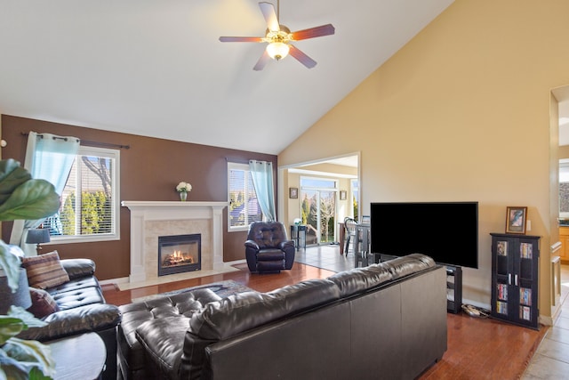 living area with high vaulted ceiling, ceiling fan, and a tiled fireplace