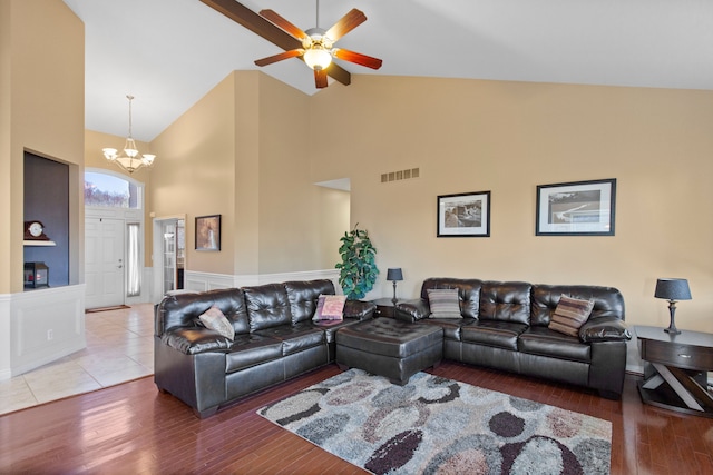 living area with wainscoting, visible vents, ceiling fan with notable chandelier, wood finished floors, and high vaulted ceiling