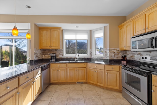 kitchen with stainless steel appliances, a sink, dark stone countertops, decorative backsplash, and hanging light fixtures