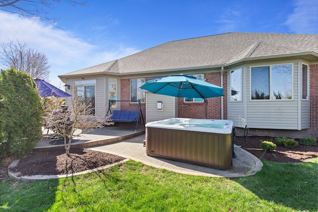 back of house featuring a lawn, brick siding, a hot tub, and a patio